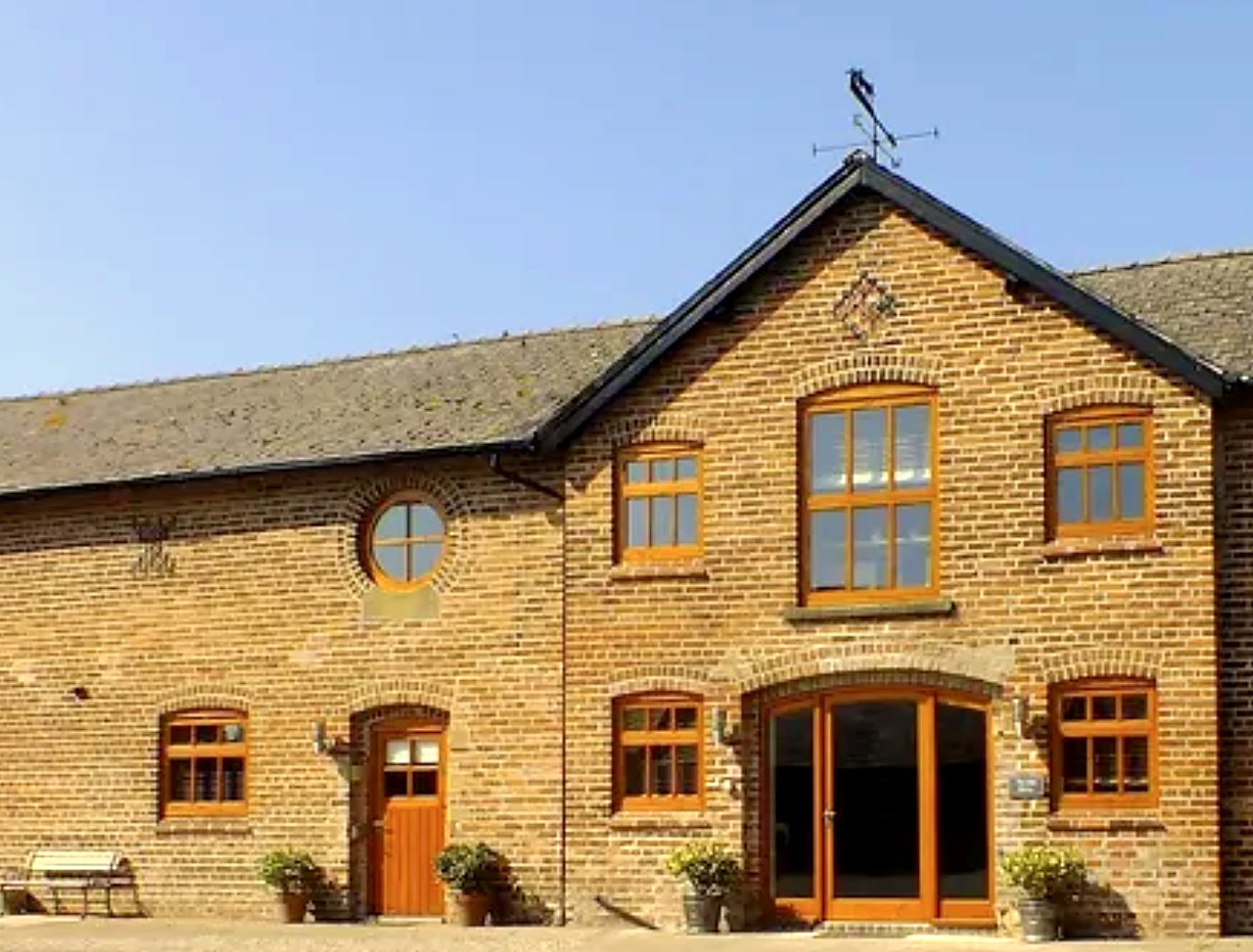 Red-brick converted barn with arched windows and a weather vane