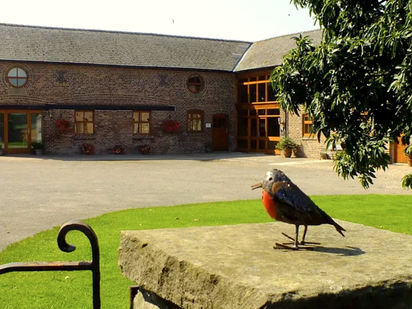 Brick farm courtyard with a robin sculpture on a stone in the foreground