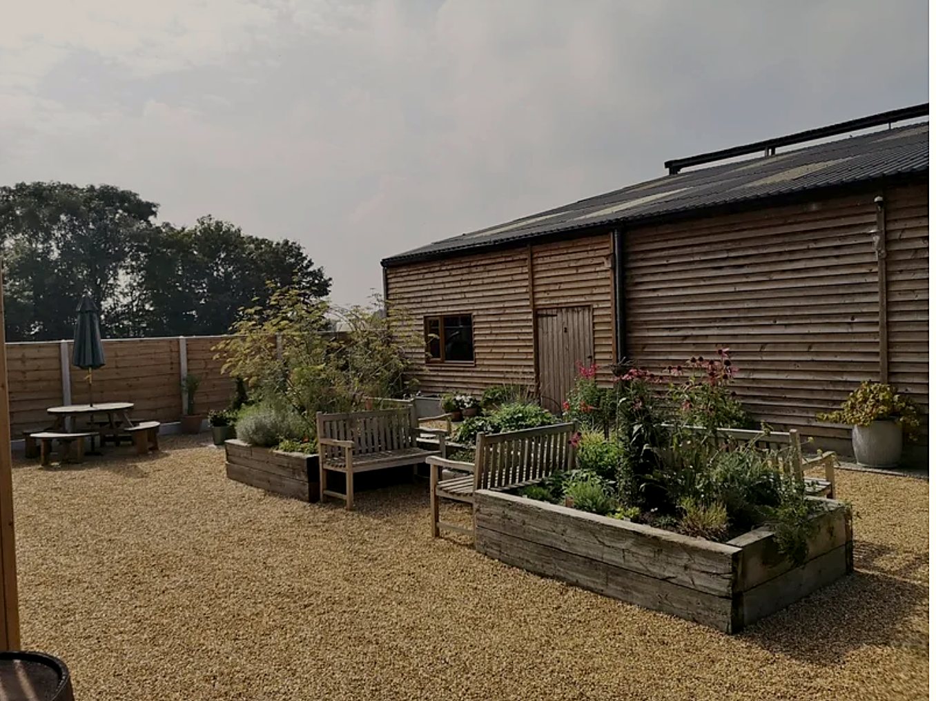 Gravel garden with raised planters, benches and a picnic table beside a timber barn
